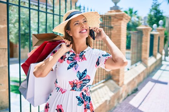 Middle age woman holding shopping bags and using smartphone at the city