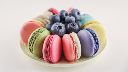 Bright colored macaroons and blueberry on round plate, tasty macarons cakes