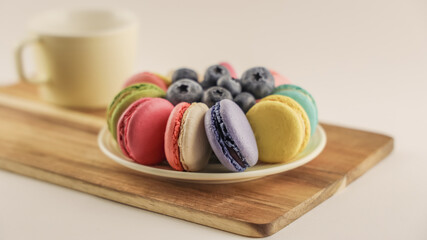 Bright colored macaroons and blueberry on round plate, tasty macarons cakes on wooden background