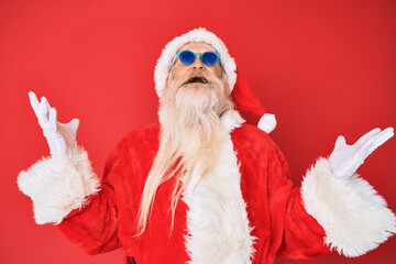 Old senior man wearing santa claus costume and sunglasses celebrating mad and crazy for success with arms raised and closed eyes screaming excited. winner concept
