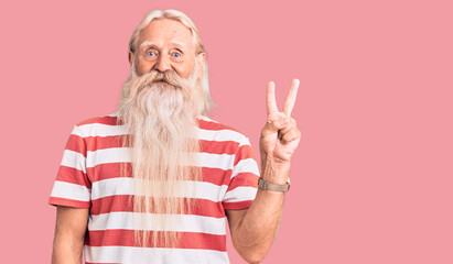 Old senior man with grey hair and long beard wearing striped tshirt showing and pointing up with fingers number two while smiling confident and happy.