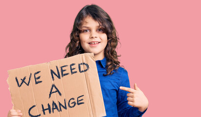 Cute hispanic child with long hair holding we need a change banner smiling happy pointing with hand and finger