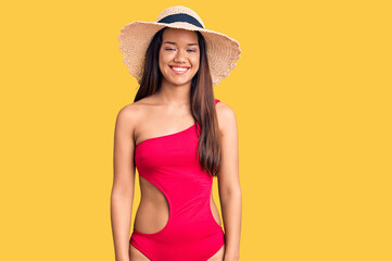 Young beautiful latin girl wearing swimwear and summer hat with a happy and cool smile on face. lucky person.
