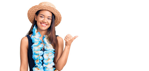 Young beautiful latin girl wearing hawaiian lei and summer hat smiling with happy face looking and...