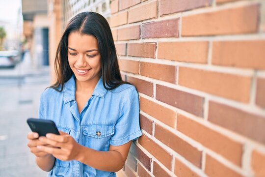 Young latin girl smiling happy using smartphone at the city.