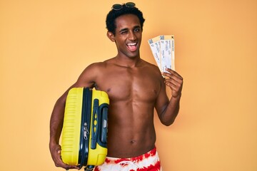 African handsome man going on summer trip holding boarding pass winking looking at the camera with...