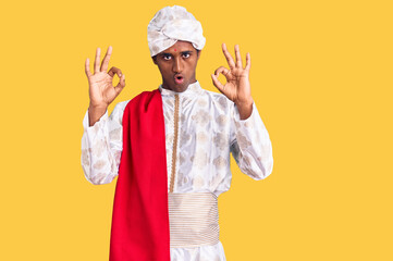 African handsome man wearing tradition sherwani saree clothes looking surprised and shocked doing...