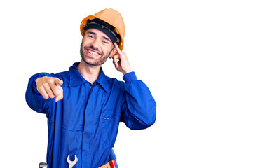 Young hispanic man wearing worker uniform smiling doing talking on the telephone gesture and pointing to you. call me.