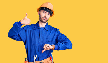 Young hispanic man wearing worker uniform doing thumbs up and down, disagreement and agreement expression. crazy conflict