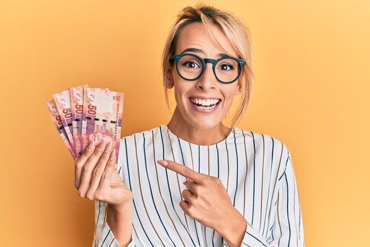 Beautiful blonde woman holding south african 50 rand banknotes smiling happy pointing with hand and finger