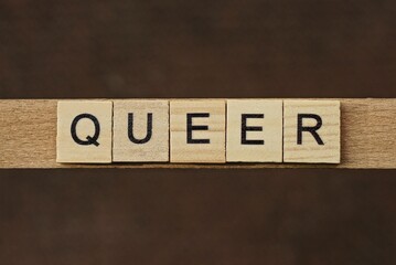 gray word queer made of wooden square letters on brown background