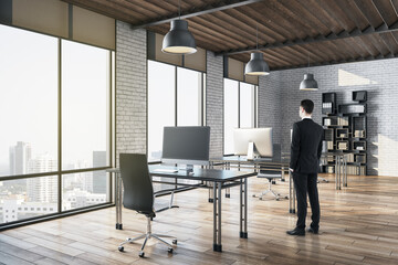 Businessman standing in modern office with rows of computer tables