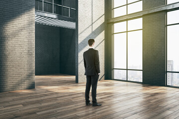 Businessman standing in gallery interior with big windows.
