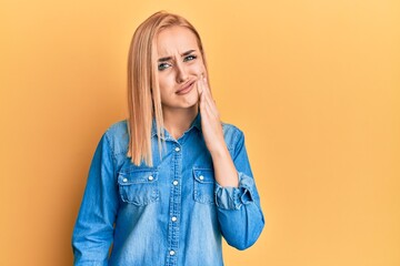 Beautiful caucasian woman wearing casual denim jacket touching mouth with hand with painful expression because of toothache or dental illness on teeth. dentist