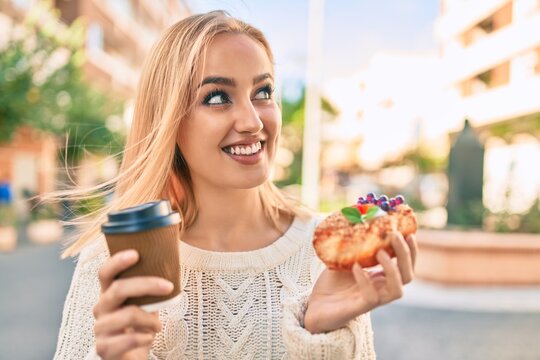 Young blonde girl smiling happy having breakfast standing at the city.