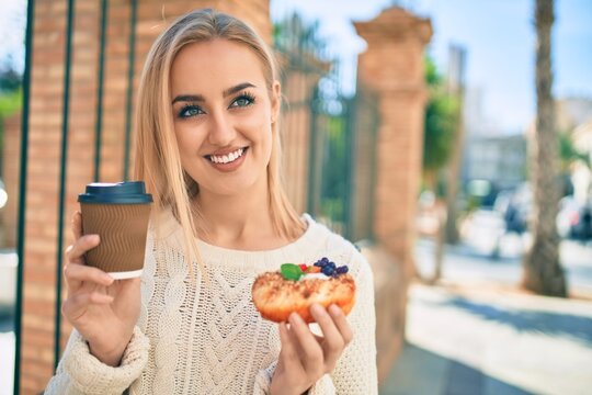 Young blonde girl smiling happy having breakfast standing at the city.