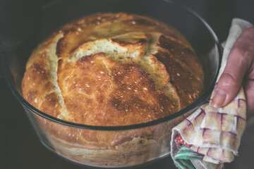Freshly baked bread straight out of the oven. Woman holding the bowl with a cloth.
