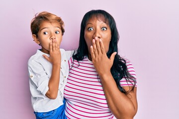 Hispanic family of mother and son hugging together with love covering mouth with hand, shocked and afraid for mistake. surprised expression