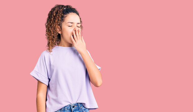 Beautiful kid girl with curly hair wearing casual clothes bored yawning tired covering mouth with hand. restless and sleepiness.