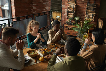 High angle portrait of multi-ethnic group of elegant young people praying with eyes closed while...