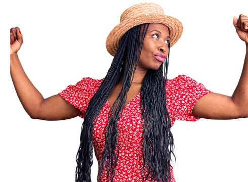 Young african american woman wearing summer hat showing arms muscles smiling proud. fitness concept.