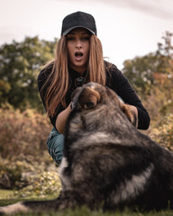 Vertical shot of a woman making a shocked expression as she is trying to pull the stick out of the dogs mouth. Playing a game of fetch and the dog wont let go of his toy