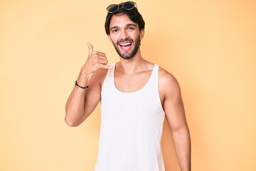 Handsome hispanic man wearing summer look and sunglasses smiling doing phone gesture with hand and fingers like talking on the telephone. communicating concepts.