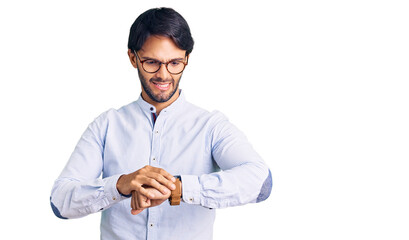 Handsome hispanic man wearing business shirt and glasses checking the time on wrist watch, relaxed...