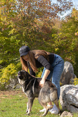 Naklejka na ściany i meble Brunette girl wearing a cap playing with a stray dog found while hiking the mountains of croatia, vertical shot of the two while the dog makes a funny playful face