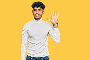 Young arab man wearing casual winter sweater showing and pointing up with fingers number five while smiling confident and happy.