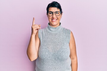 Plus size brunette woman wearing casual clothes and glasses pointing finger up with successful idea. exited and happy. number one.