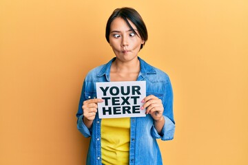 Beautiful young woman with short hair holding your text here message making fish face with mouth and squinting eyes, crazy and comical.