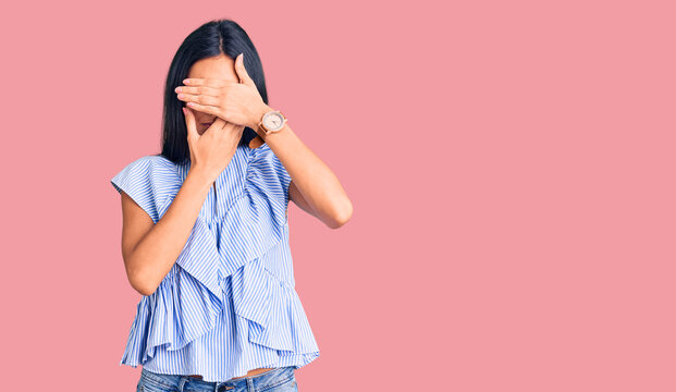 Young beautiful latin girl wearing casual clothes covering eyes and mouth with hands, surprised and shocked. hiding emotion
