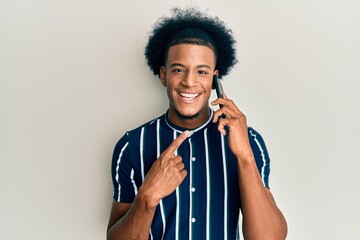 African american man with afro hair having conversation talking on the smartphone smiling happy pointing with hand and finger