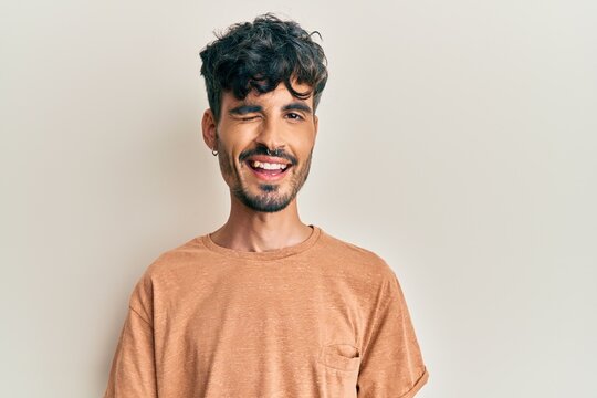 Young hispanic man wearing casual clothes winking looking at the camera with sexy expression, cheerful and happy face.