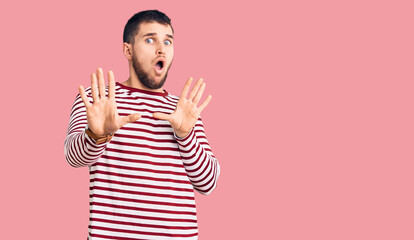 Young handsome man wearing striped sweater moving away hands palms showing refusal and denial with...