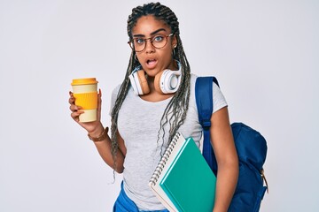 Young african american woman with braids wearing student backpack drinking coffee in shock face,...