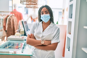Young african american woman smiling happy working at the till wearing coronavirus safety mask at...