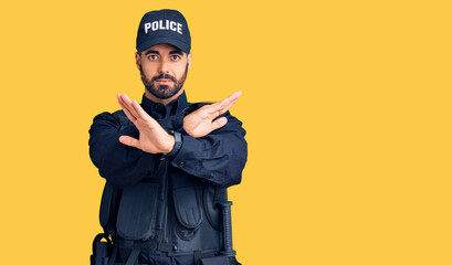 Young hispanic man wearing police uniform rejection expression crossing arms and palms doing negative sign, angry face