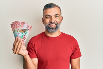 Middle age handsome man holding 100 new zealand dollars banknote looking positive and happy standing and smiling with a confident smile showing teeth