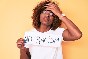Young african american woman holding no racism banner stressed and frustrated with hand on head,...