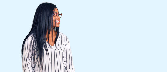 Young african american woman wearing casual clothes and glasses looking away to side with smile on face, natural expression. laughing confident.