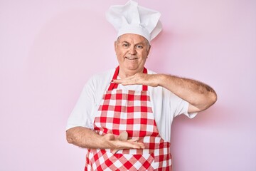 Senior grey-haired man wearing professional baker apron gesturing with hands showing big and large size sign, measure symbol. smiling looking at the camera. measuring concept.