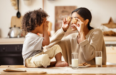 happy african american family: mother and little son eat cookies with milk at home.