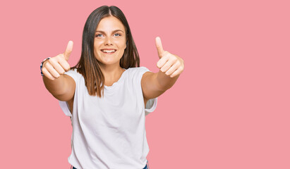 Young caucasian woman wearing casual white tshirt approving doing positive gesture with hand, thumbs up smiling and happy for success. winner gesture.