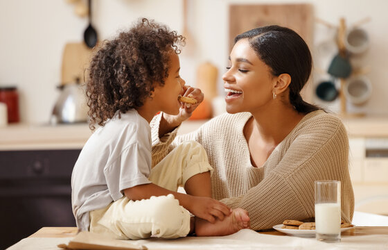 happy african american family: mother and little son eat cookies with milk at home.