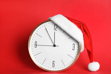 Clock with Santa hat showing five minutes until midnight on red background. New Year countdown