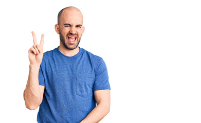 Young handsome man wearing casual t shirt smiling with happy face winking at the camera doing victory sign. number two.