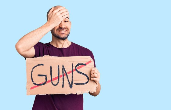 Young handsome man holding prohibited guns banner stressed and frustrated with hand on head, surprised and angry face