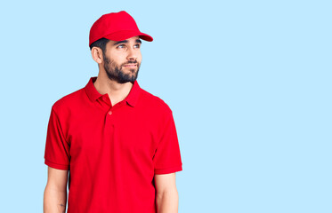 Young handsome man with beard wearing delivery uniform smiling looking to the side and staring away thinking.